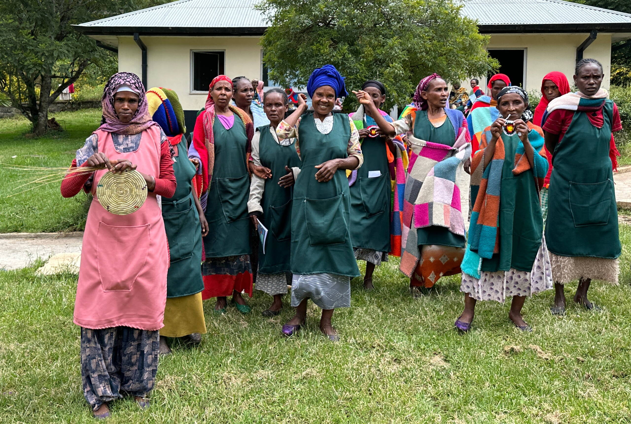 Wiedereingliederung Eine Gruppe Frauen steht vor einem Haus mit Wellblech. Alle halten handwerkliche Arbeiten in die Höhe.