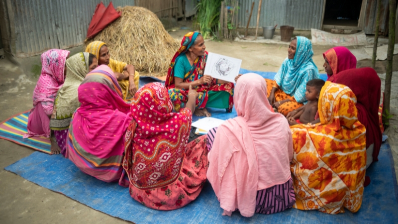 Frauen mit Fisteln schaffen sich Perspektiven Frauen sitzen am Boden im Kreis, eine Frau erklärt etwas und hält eine Grafik in den Händen.