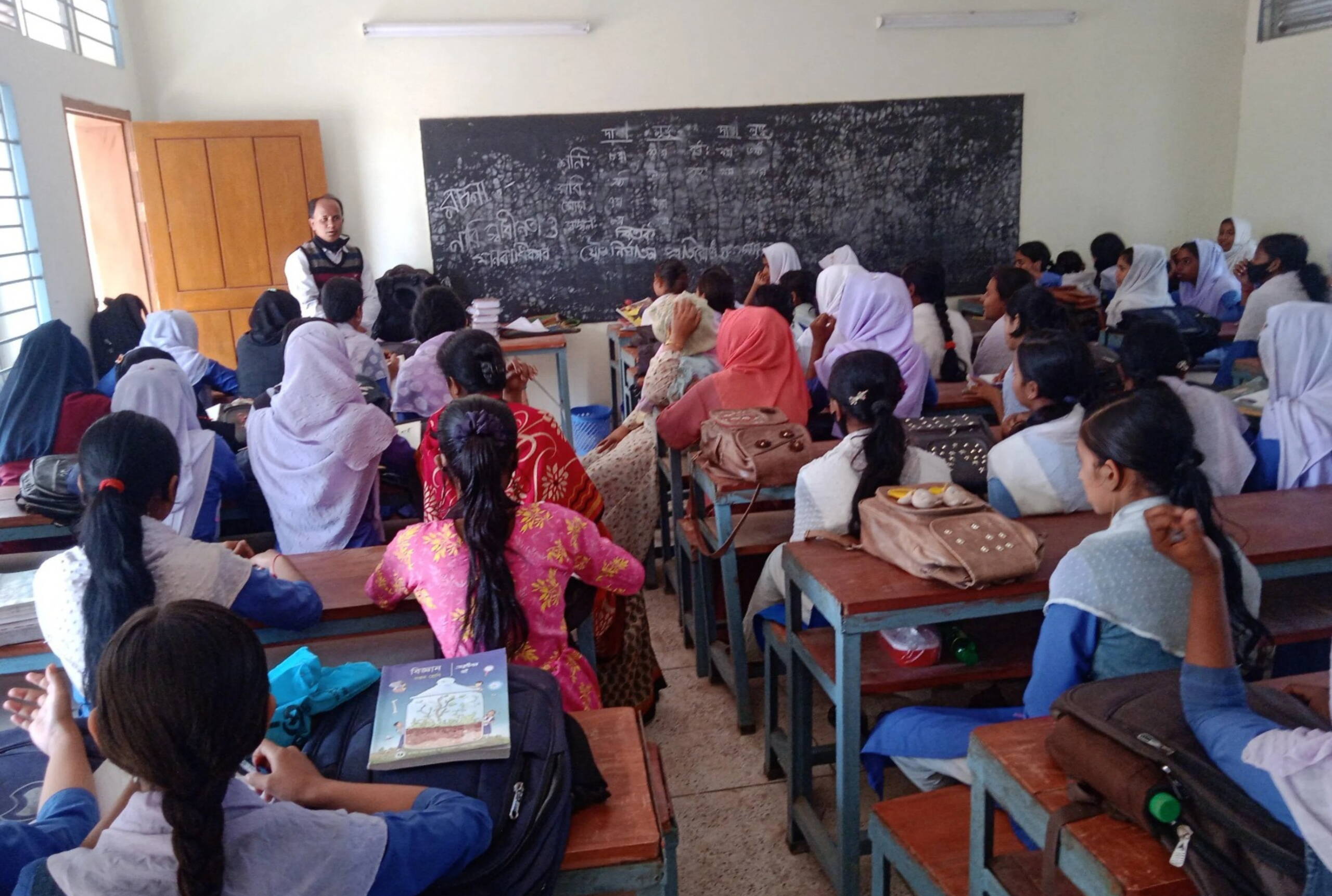 Fistelaufklärung Ein Lehrer steht vor einer Klasse mit Mädchen und erklärt etwas.
