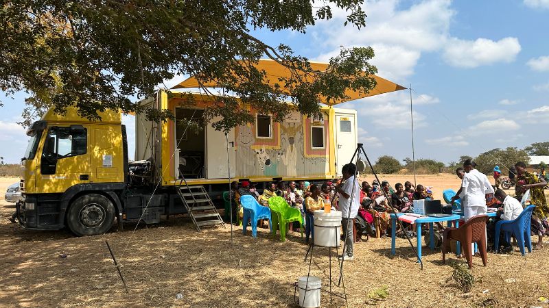 Die mobile Klinik von NURU wird Teil von Women’s Hope Bunt angemalter Lastwagen mit Sonnendach, davor Menschen auf Stühlen.