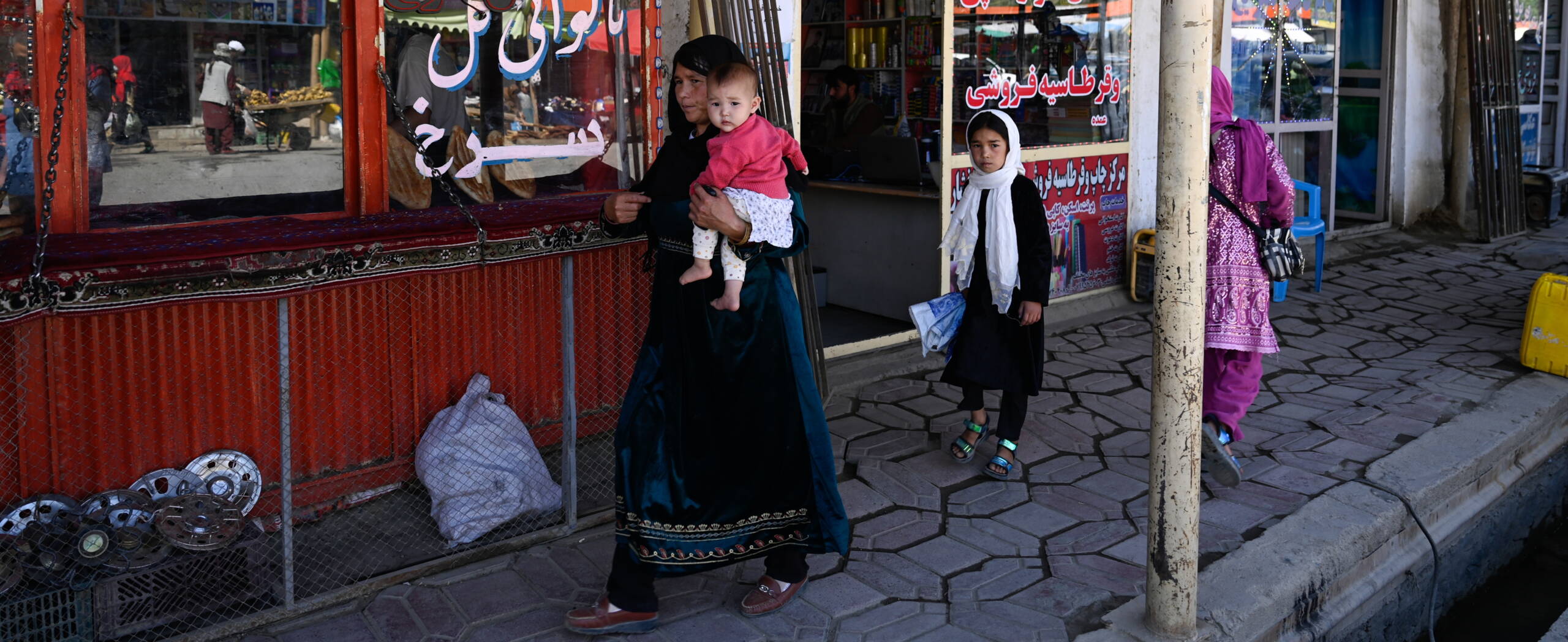 Strassenszene Afghanistan Eine Frau läuft mit zwei Kindern eine Einkaufsstrasse entlang.